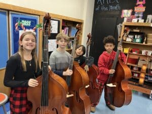 Four students get ready to play their double basses in music class